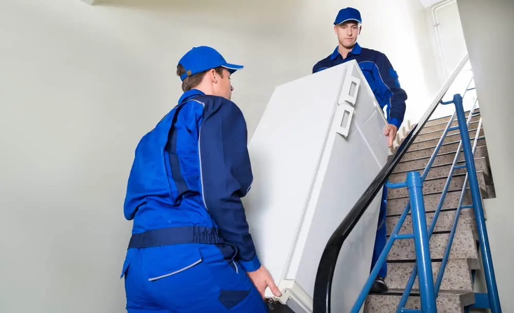 Deux manutentionnaires descendant un réfrigérateur dans la cage d'escalier d'un immeuble sans ascenseur